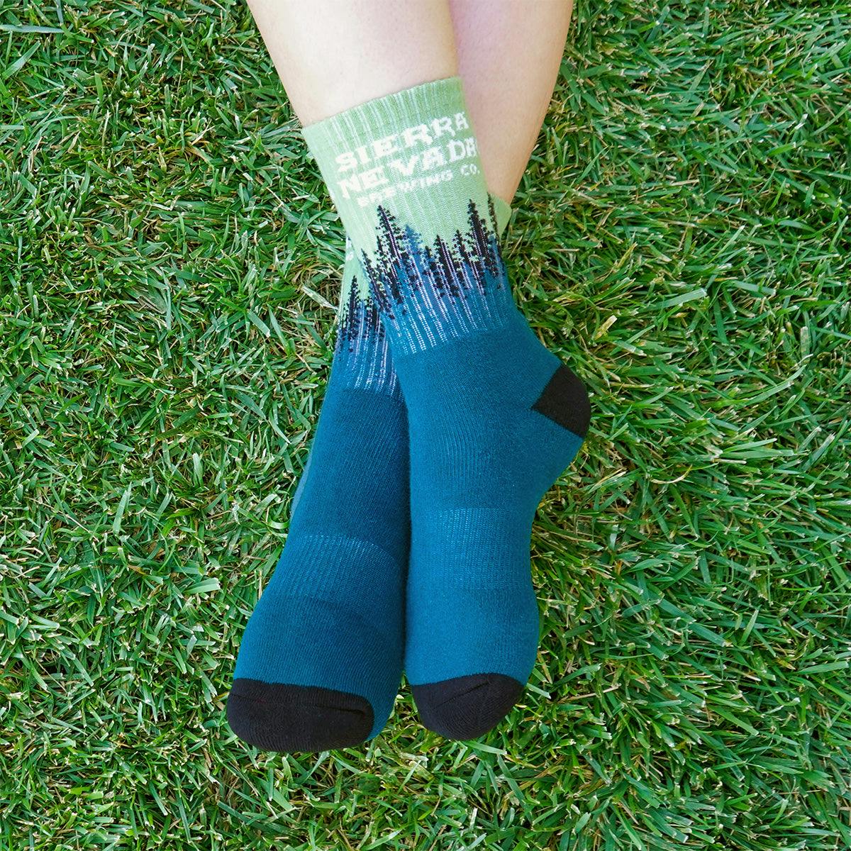 A person wears a pair of the Sierra Nevada Treeline Socks while sitting on a grassy area