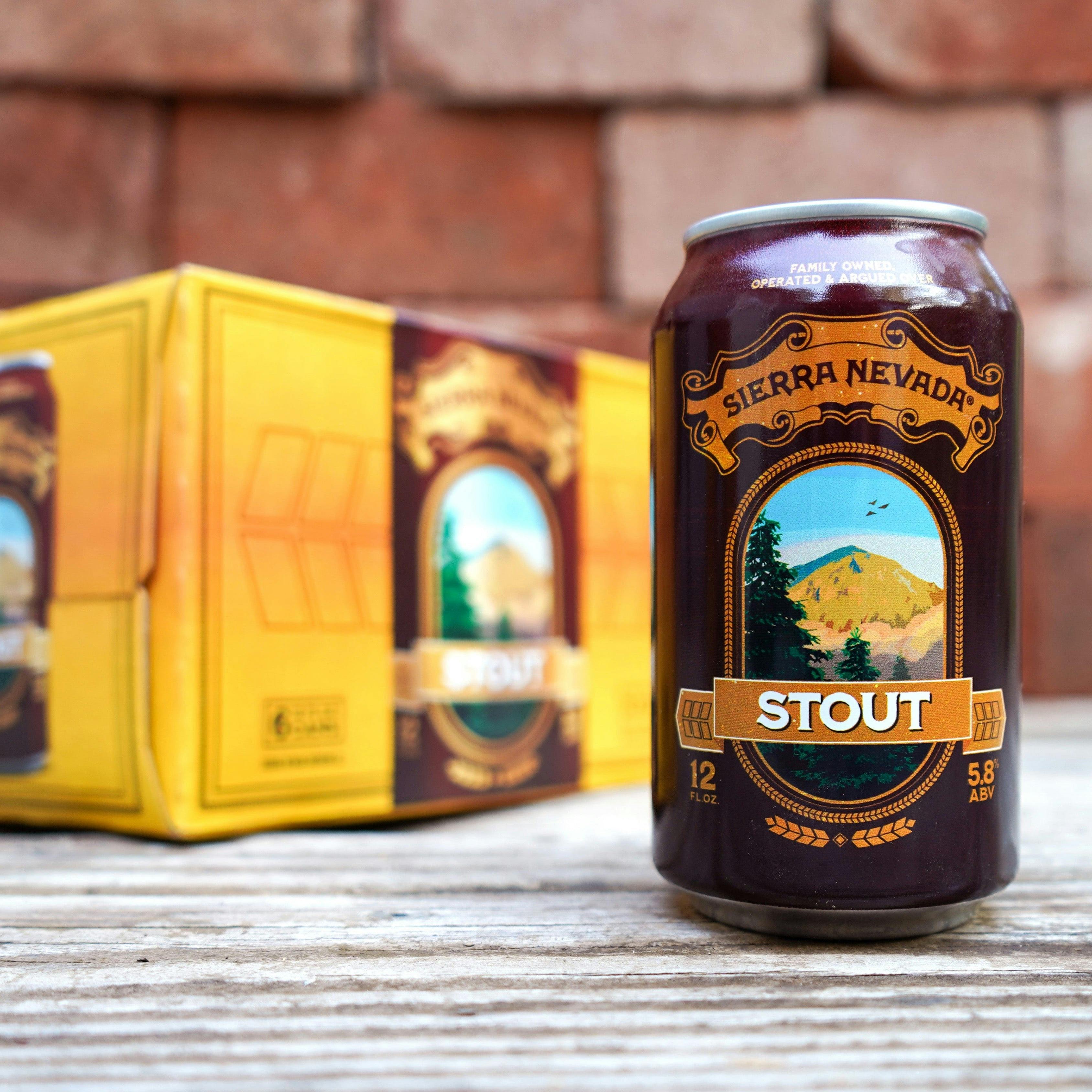 A 12oz can of Sierra Nevada Stout sits in the foreground on a wooden tabletop with the 6-pack box in the background