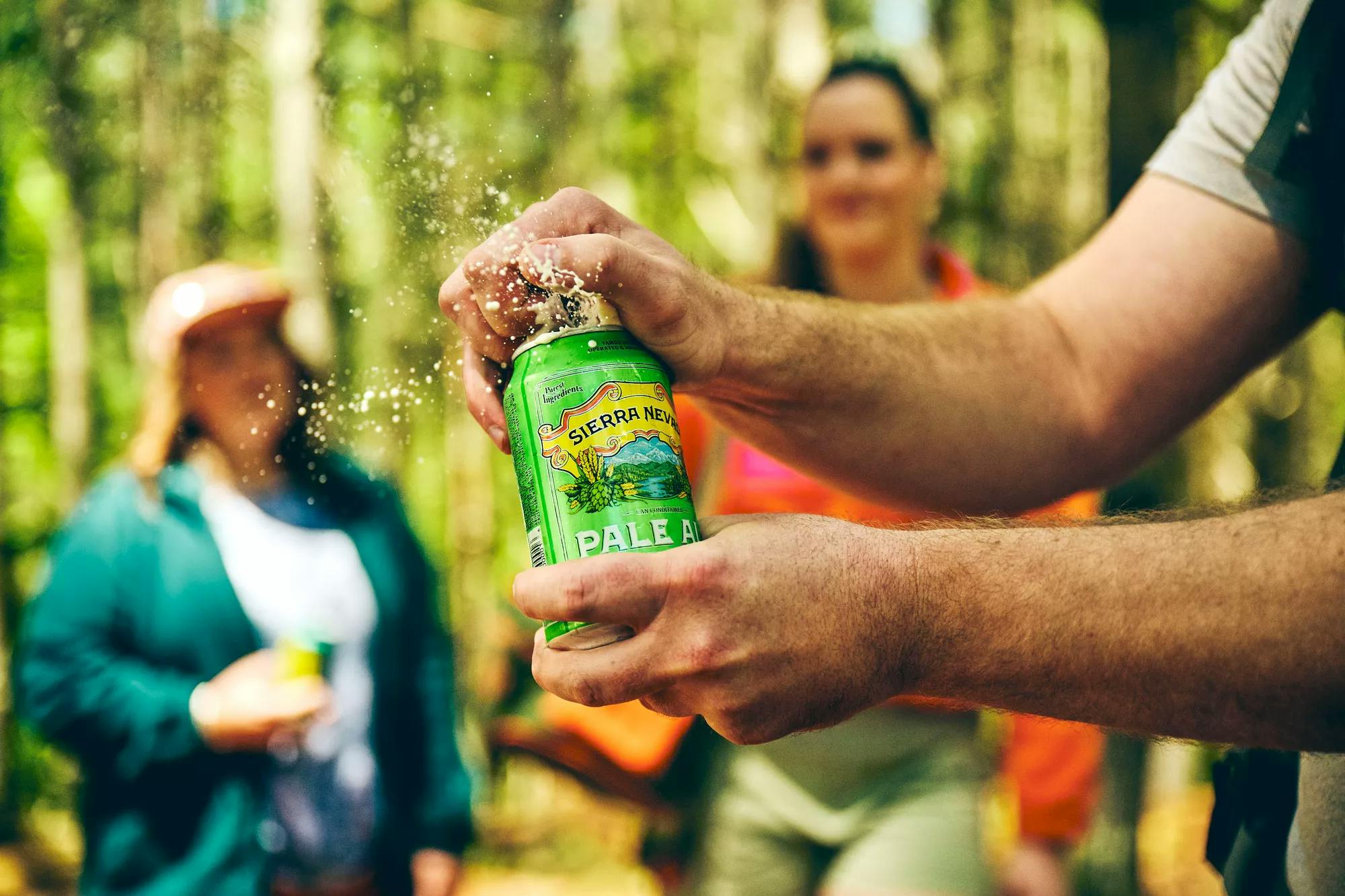 A cold can of Pale Ale is cracked open by a hiker surrounded by friends outdoors.