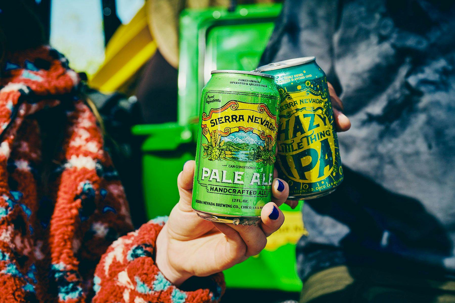 Two people raising cans of Sierra Nevada Pale Ale and Hazy Little Thing to cheers