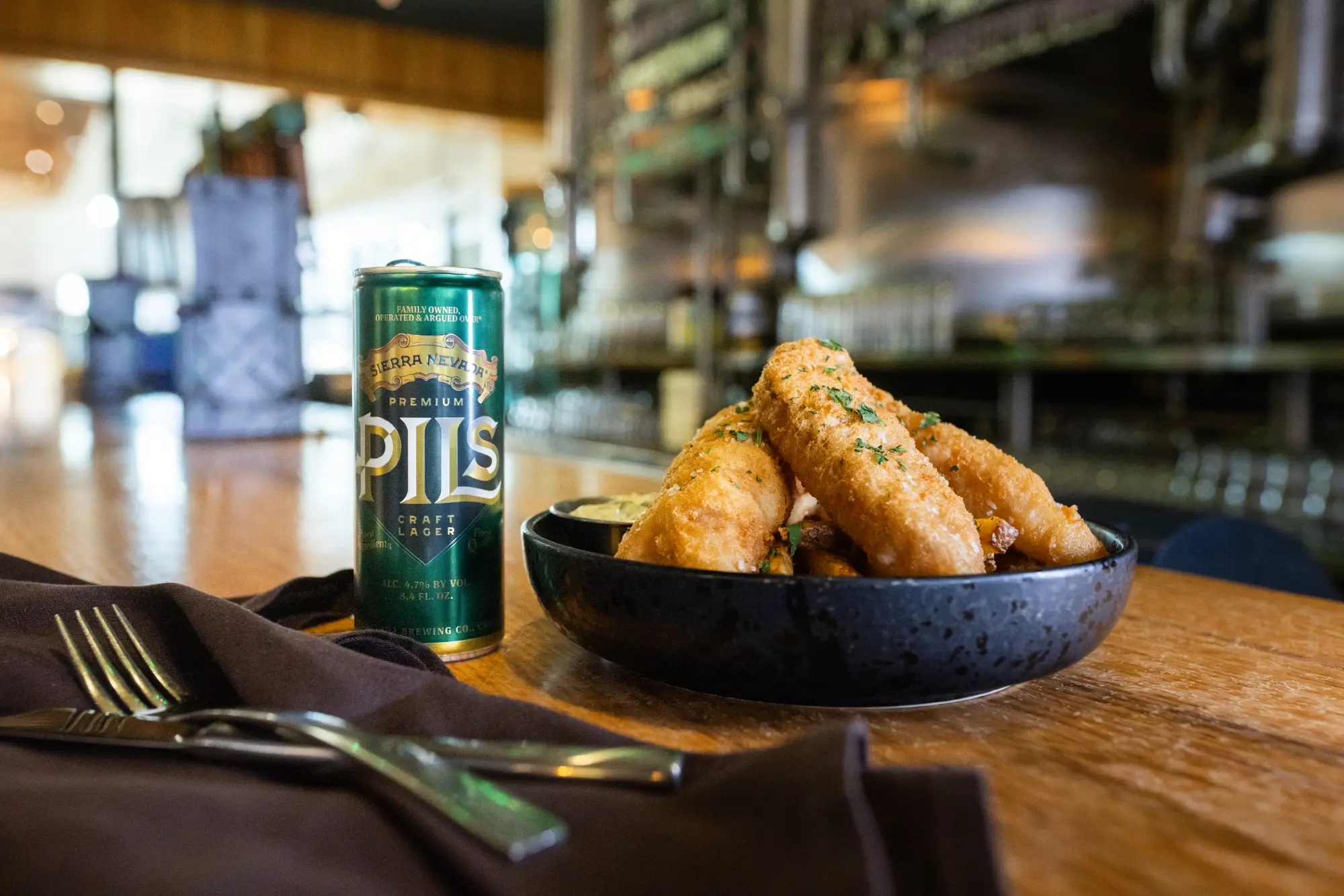 Can of PILS on table next to bowl of fish and chips.